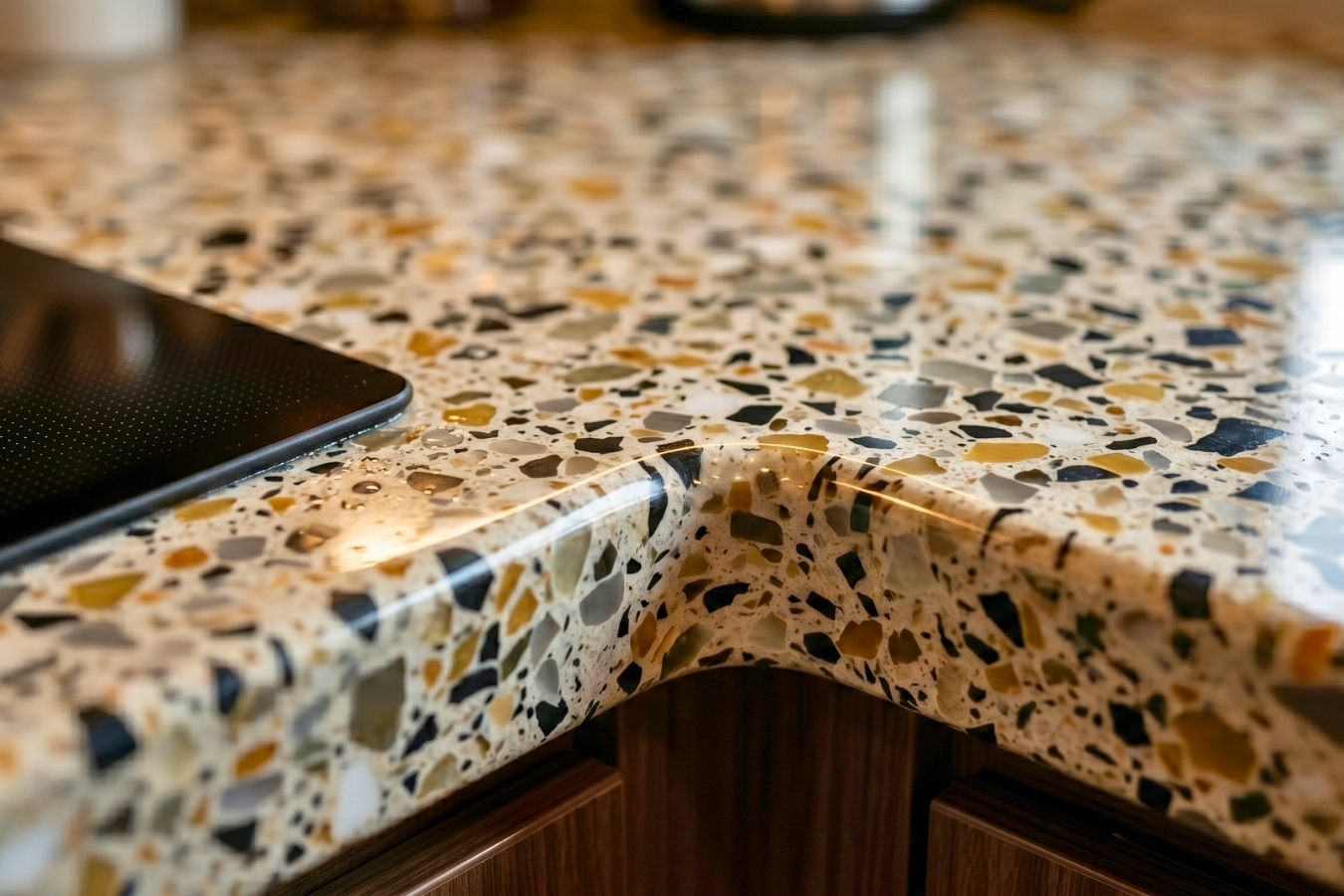 Close-up of a curved solid surface countertop edge with a multi-color terrazzo pattern; illustrating seamless fabrication achieved with Marktec color-matched adhesives and specialized aggregate chips.