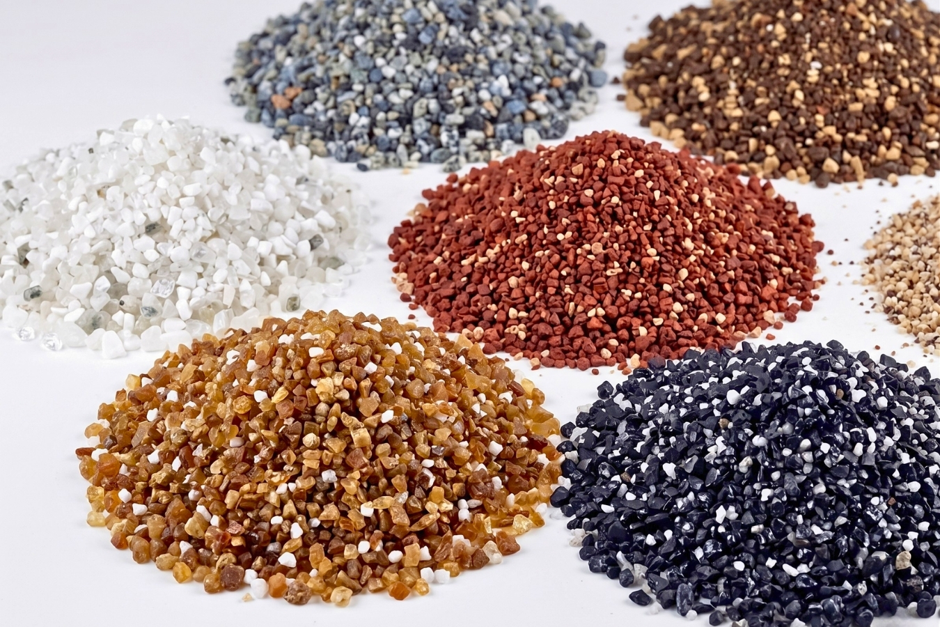 A diverse collection of decorative solid surface chips and aggregate samples in multiple colors (terracotta, blue-grey, white, black/speckled, gold/amber) manufactured by Marktec for custom countertop designs.